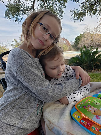 Sophia being hugged by her sister outdoors